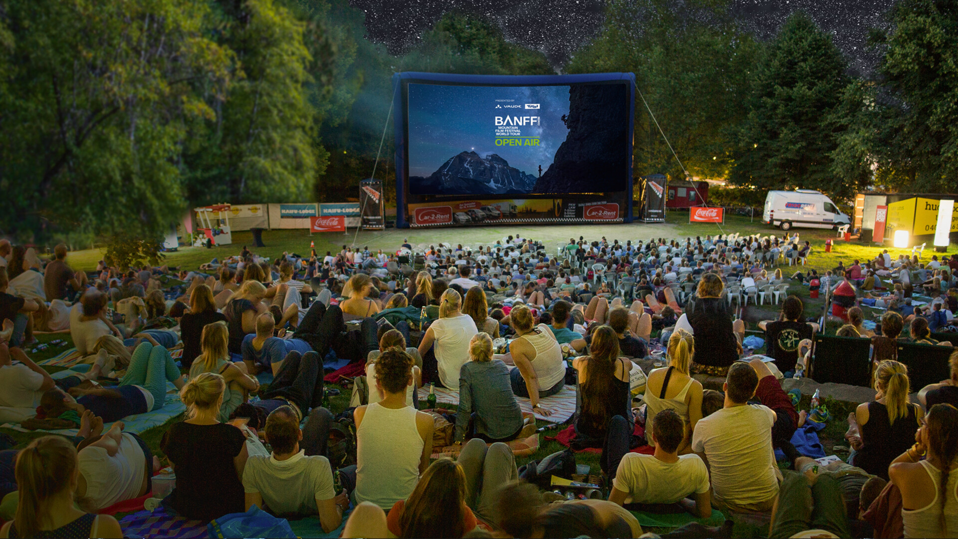 Open-Air-Publikum auf einer Wiese vor einer aufblasbaren Leinwand der Banff Tour bei einer Vorf&uuml;hrung unter freiem Sternenhimmel.