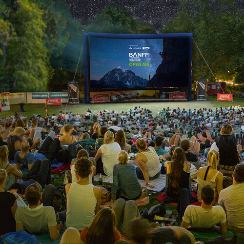 Open-Air-Publikum auf einer Wiese vor einer aufblasbaren Leinwand der Banff Tour bei einer Vorf&uuml;hrung unter freiem Sternenhimmel.