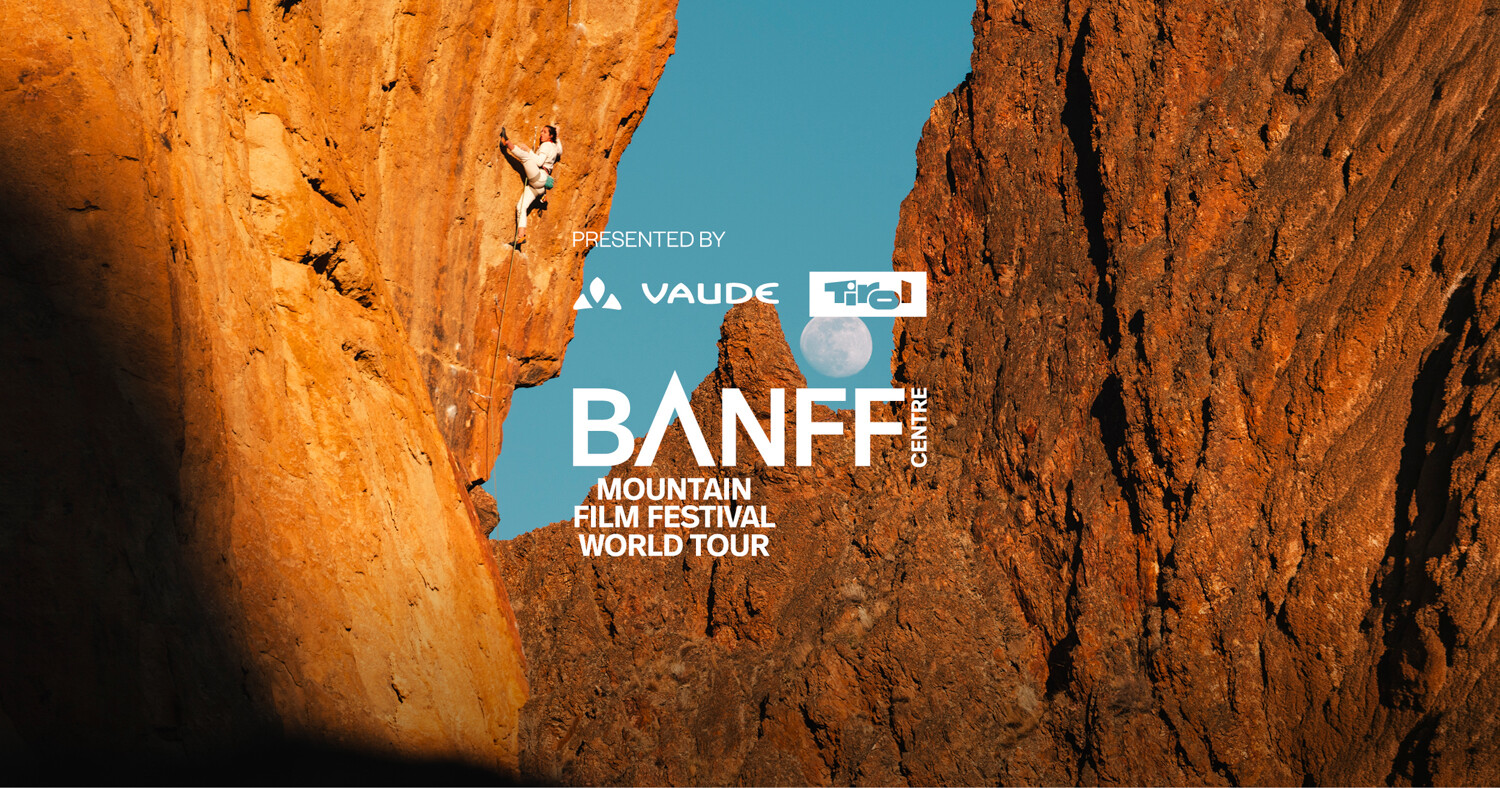 Banff Tour 2027 &ndash; Kletterer:in an einer steil &uuml;berh&auml;ngenden, orange leuchtenden Felswand, im Hintergrund der Vollmond &uuml;ber zerkl&uuml;fteten Felst&uuml;rmen vor blauem Himmel.