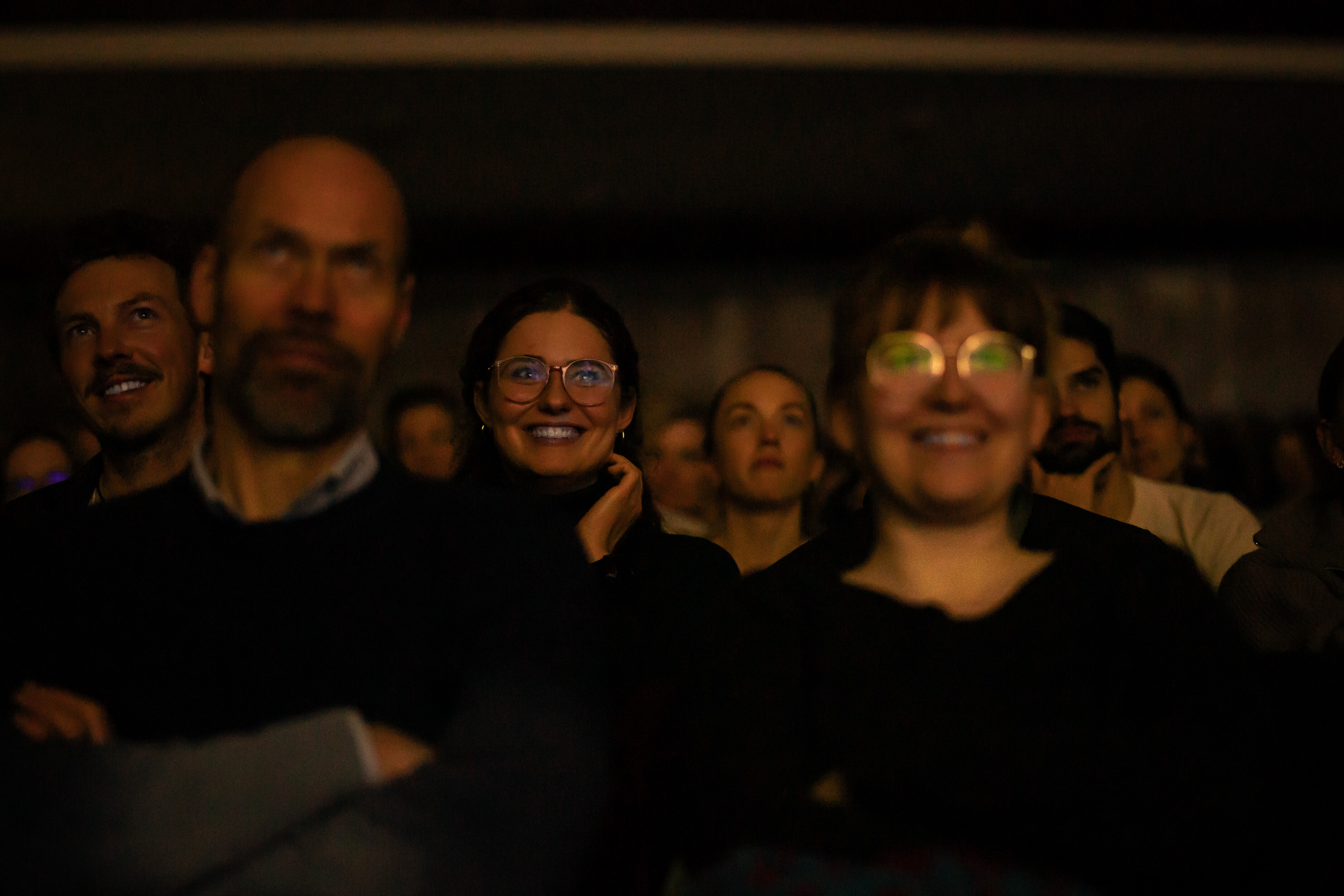 Audience at a Banff Tour event, lit by the glow of the screen, smiling toward the stage.