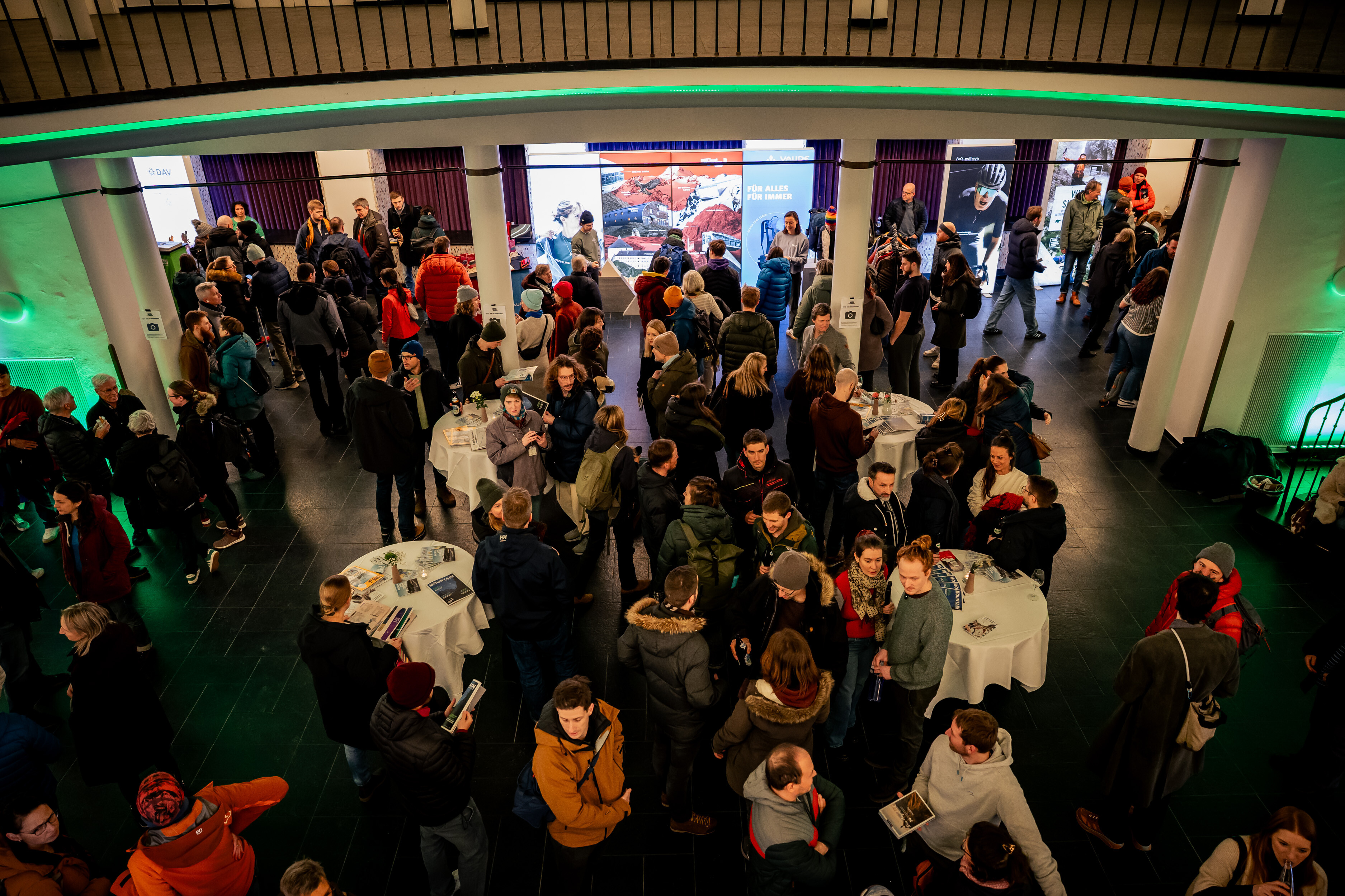 Audience mingling at standing tables and partner booths in the foyer of the Alte Kongresshalle in Munich during a Banff Tour event.