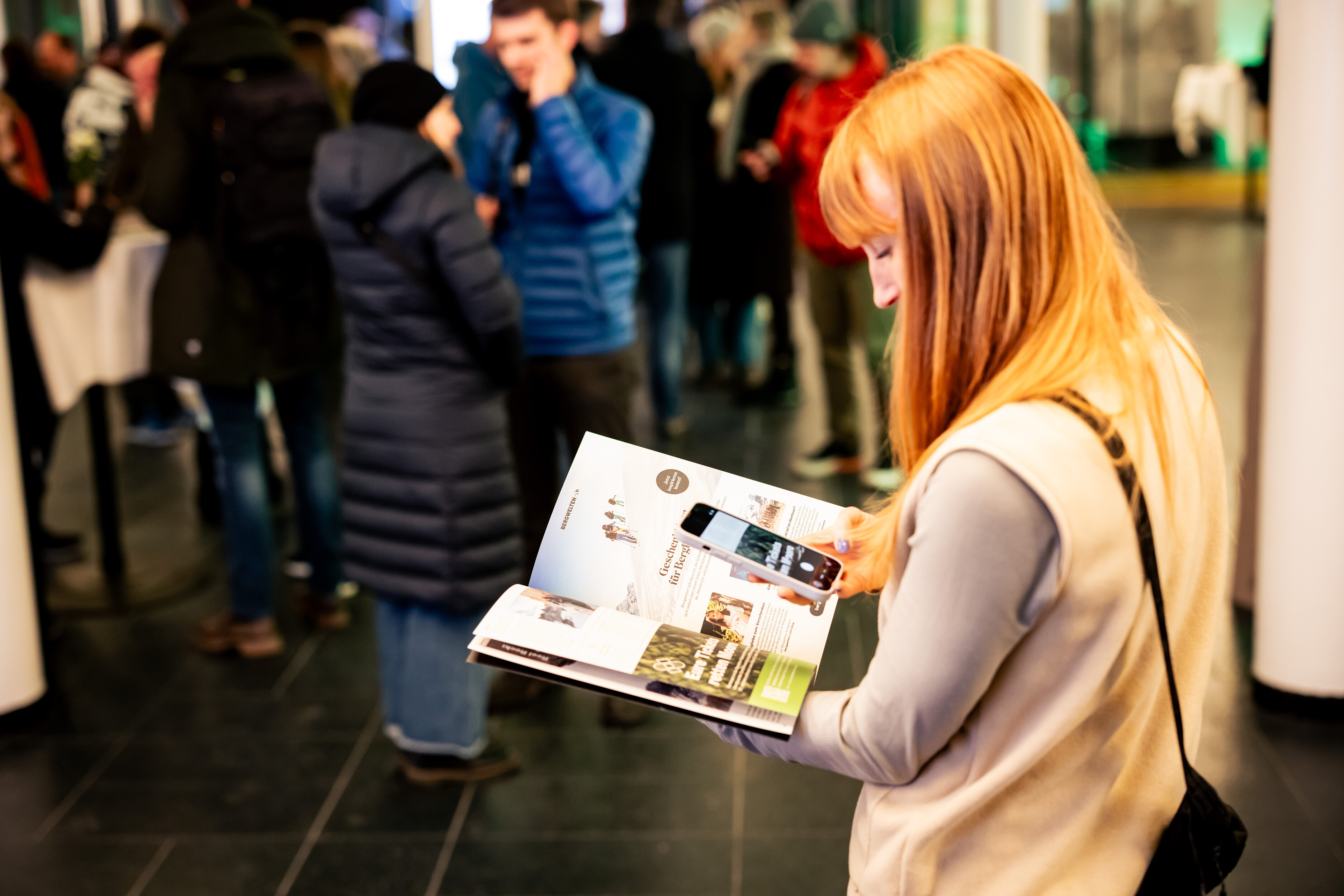 Visitor leafing through a magazine and scanning a page with her smartphone in the foyer of a Banff Tour event.