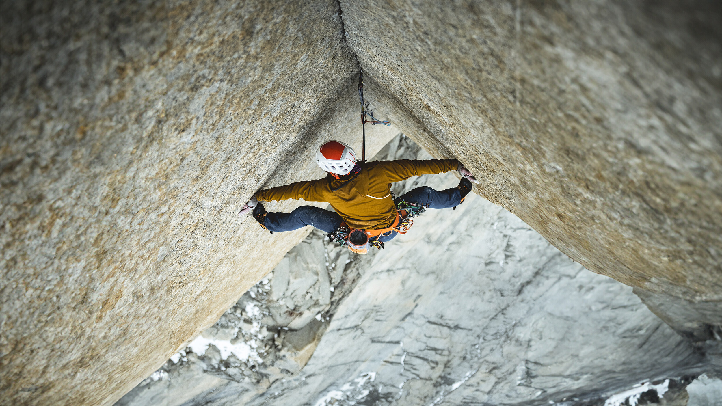 Kletterer Siebe Vanhee in einem Riss einer &uuml;berh&auml;ngenden Granitwand der Route Riders on the Storm in Patagonien, von oben fotografiert, im Hintergrund tief verschneite Felsen.